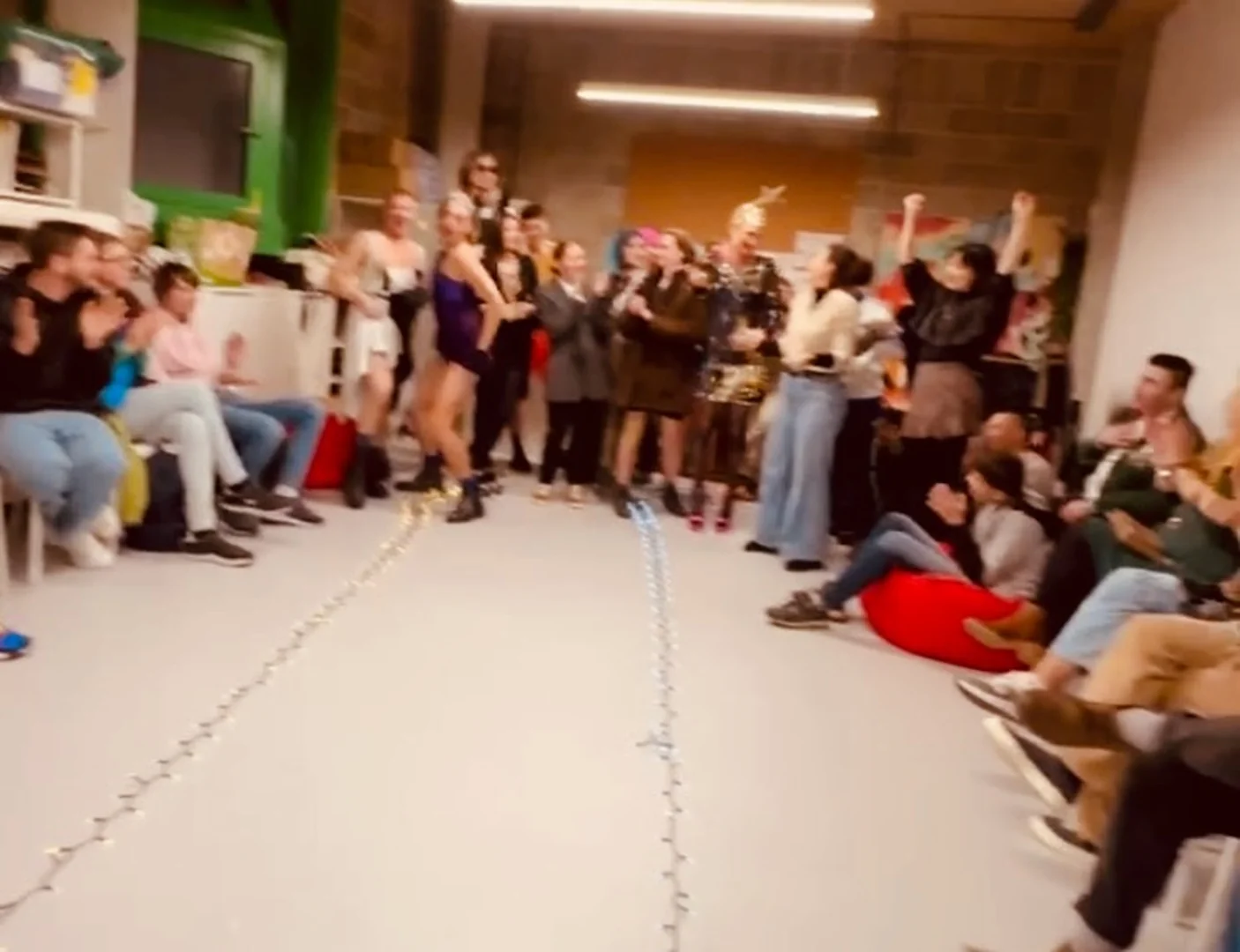 Participants line the sides of a room, clapping and celebrating as someone takes the floor.